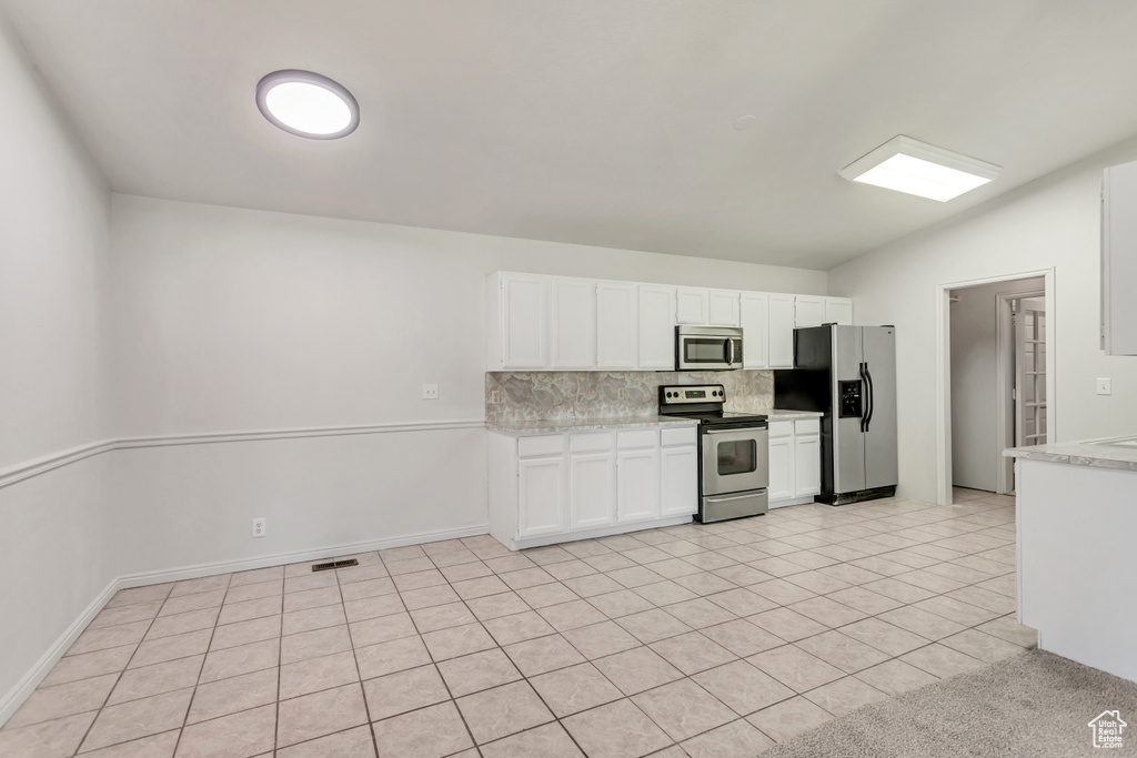 Kitchen featuring backsplash, vaulted ceiling, stainless steel appliances, white cabinets, and light tile floors