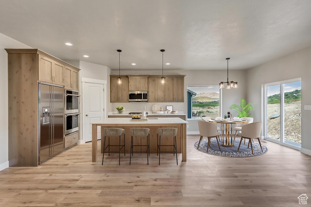 Kitchen featuring a center island with sink, hanging light fixtures, appliances with stainless steel finishes, and light wood-type flooring