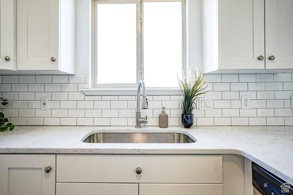 Kitchen featuring light stone counters, white cabinets, sink, backsplash, and dishwashing machine