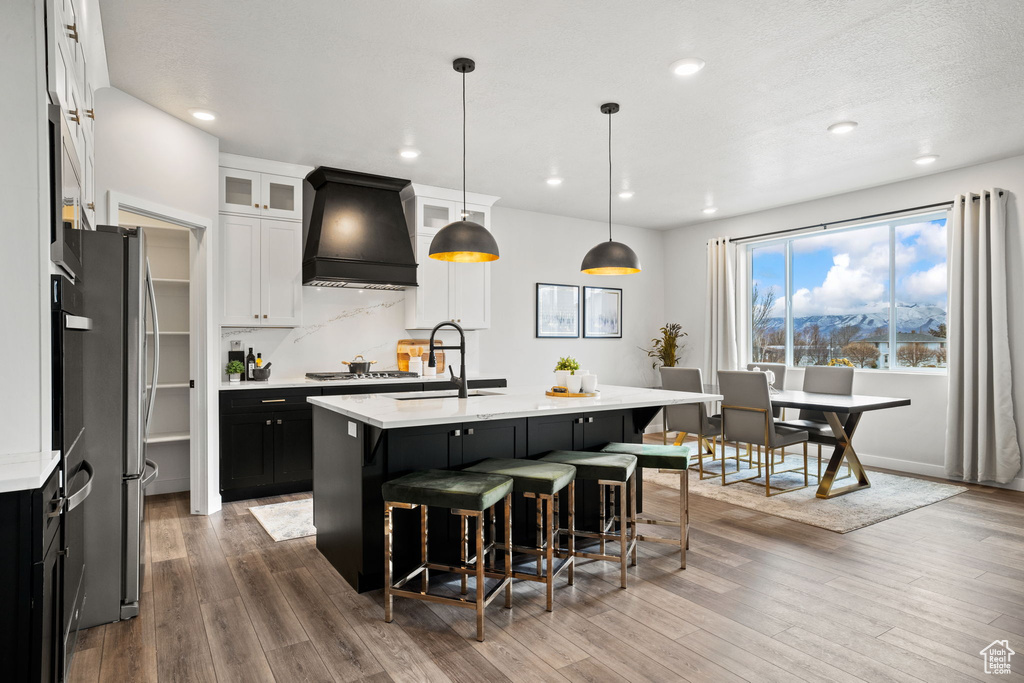 Kitchen featuring decorative light fixtures, premium range hood, a breakfast bar area, hardwood / wood-style flooring, and a kitchen island with sink