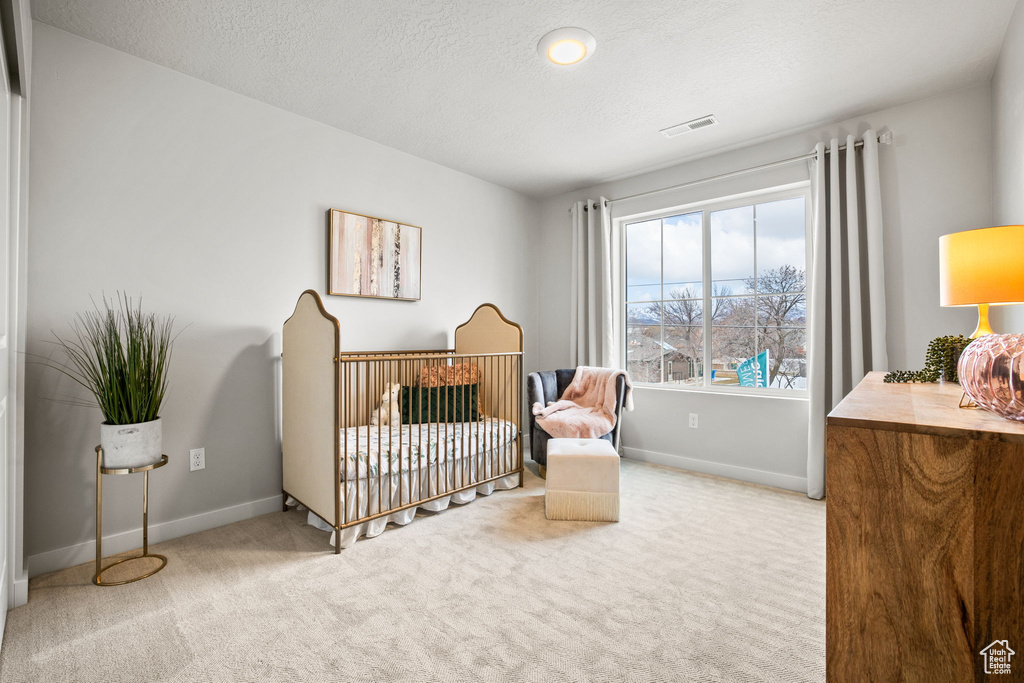 Bedroom with light carpet, a crib, and a textured ceiling