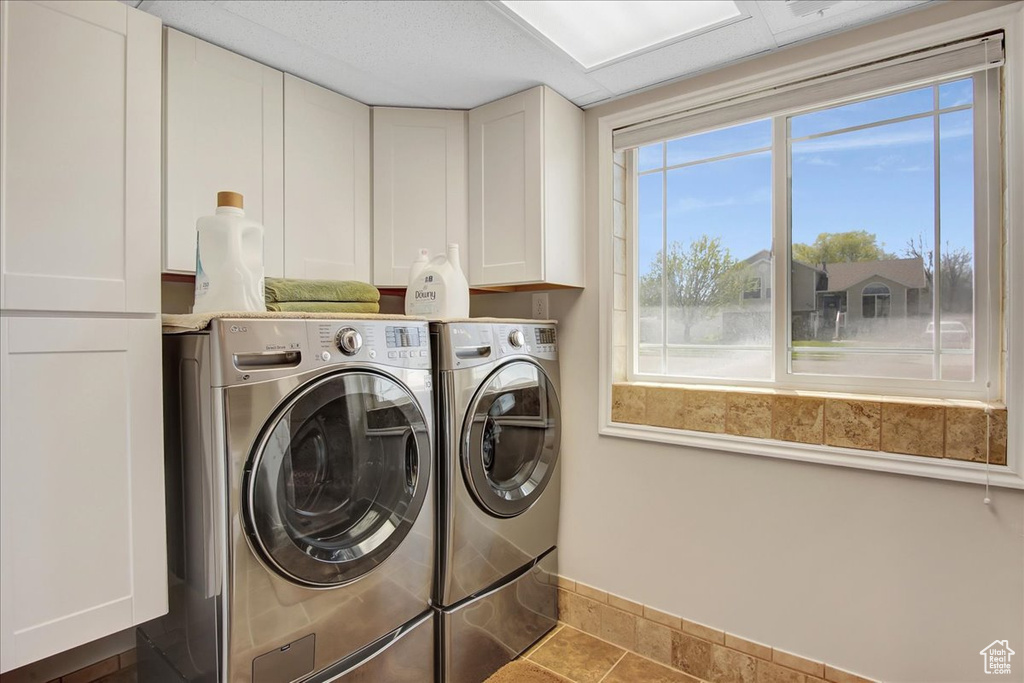 Laundry room featuring a wealth of natural light, cabinets, dark tile flooring, and washing machine and dryer