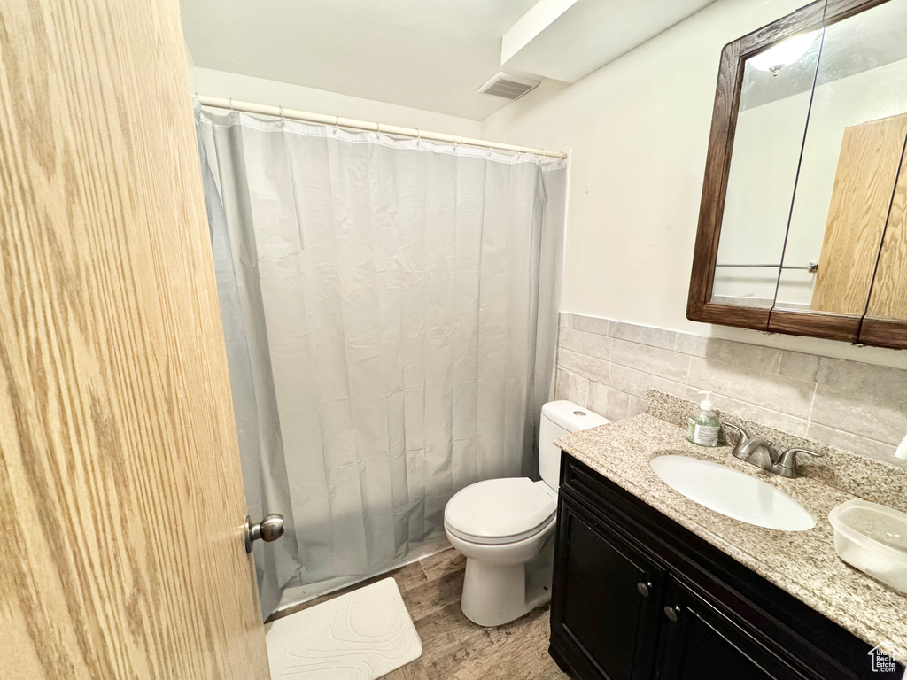 Bathroom featuring tasteful backsplash, wood-type flooring, oversized vanity, and toilet