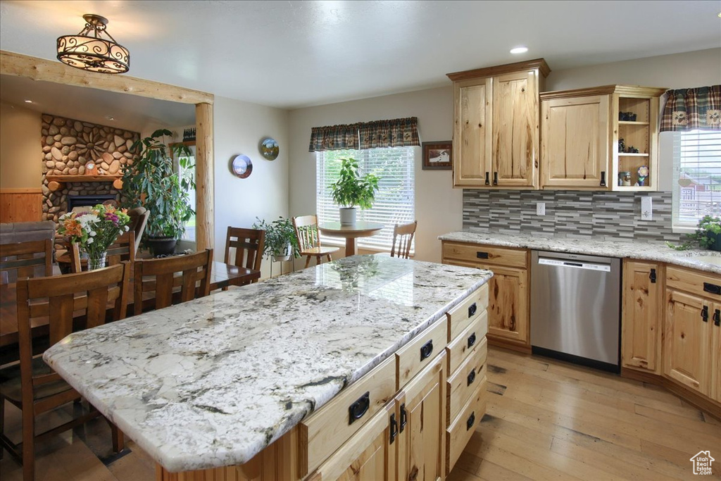 Kitchen with a fireplace, light wood-type flooring, a kitchen island, tasteful backsplash, and dishwasher