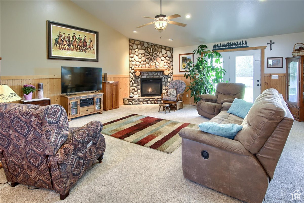 Carpeted living room featuring vaulted ceiling, ceiling fan, and a stone fireplace