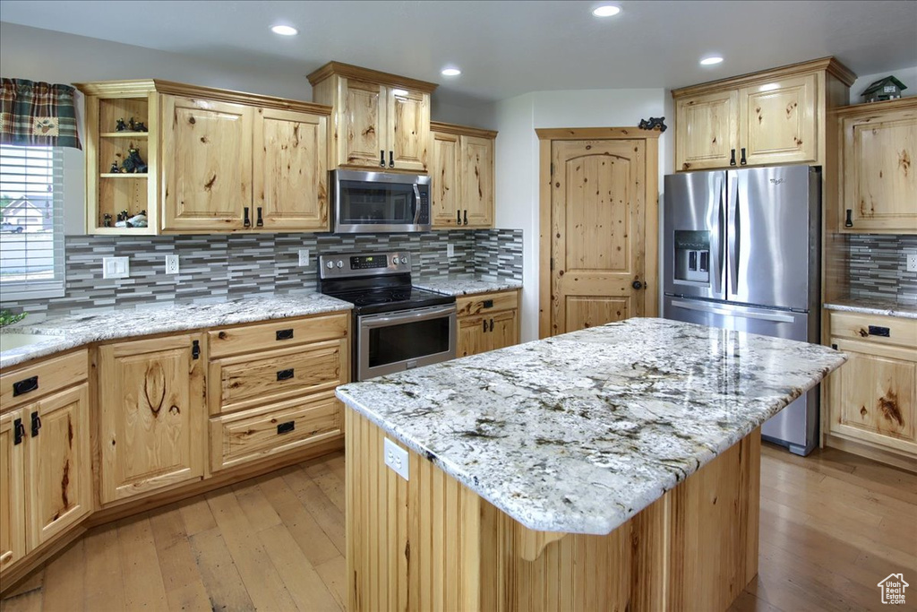 Kitchen with a center island, appliances with stainless steel finishes, light hardwood / wood-style flooring, and backsplash