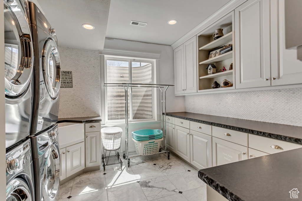 Kitchen with white cabinets, tasteful backsplash, light tile floors, and stacked washer / dryer