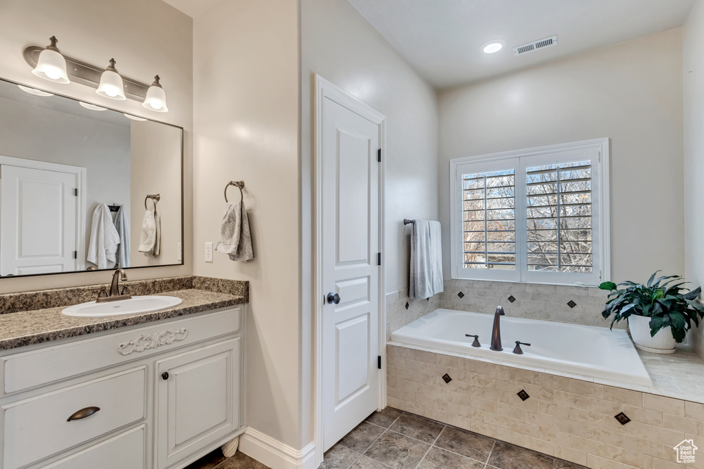 Bathroom featuring tile floors, vanity with extensive cabinet space, and tiled tub