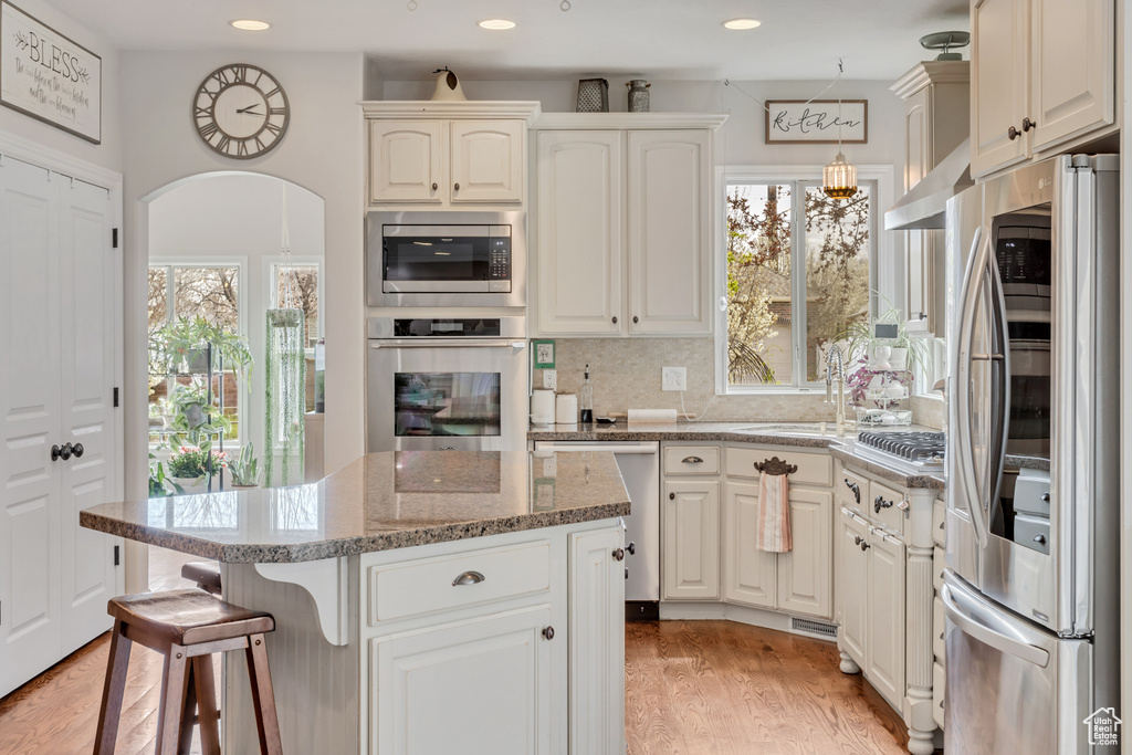 Kitchen featuring appliances with stainless steel finishes, light hardwood / wood-style flooring, tasteful backsplash, white cabinetry, and a center island