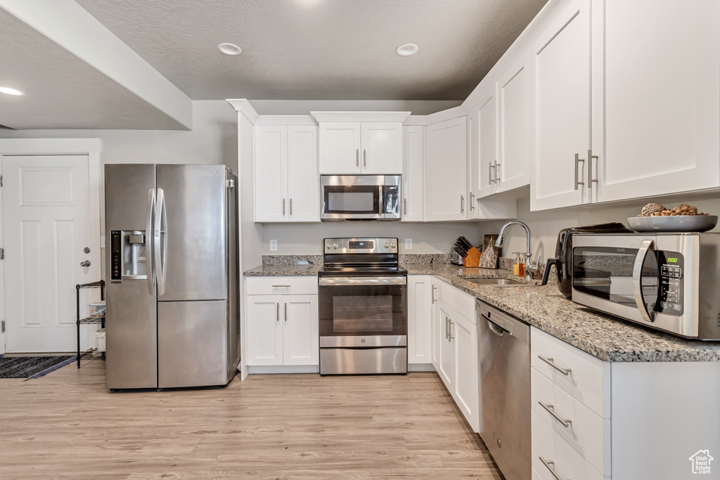 Kitchen featuring appliances with stainless steel finishes, light hardwood / wood-style flooring, light stone counters, white cabinets, and sink