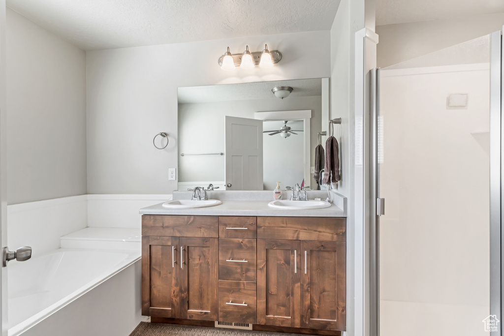 Bathroom featuring a bath to relax in, vanity with extensive cabinet space, ceiling fan, and double sink