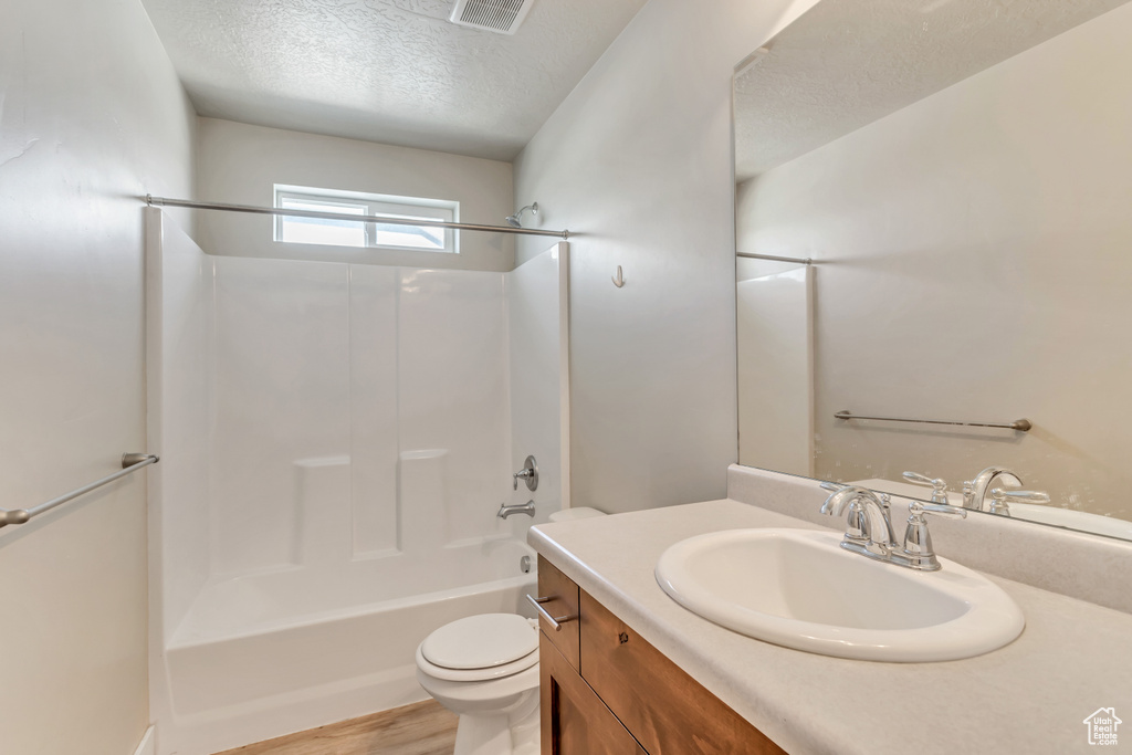Full bathroom featuring a textured ceiling, shower / bathing tub combination, toilet, wood-type flooring, and vanity