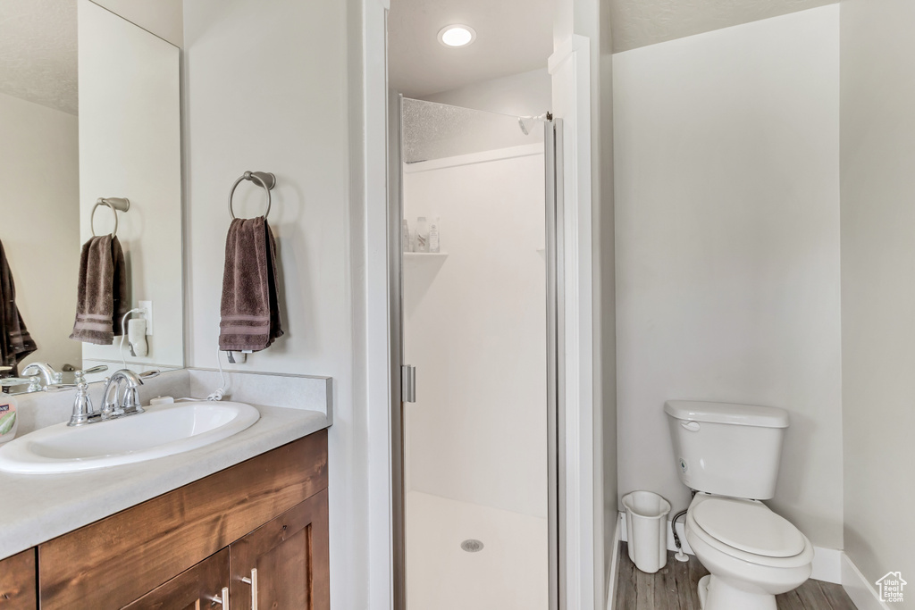 Bathroom with vanity with extensive cabinet space, toilet, walk in shower, and hardwood / wood-style flooring