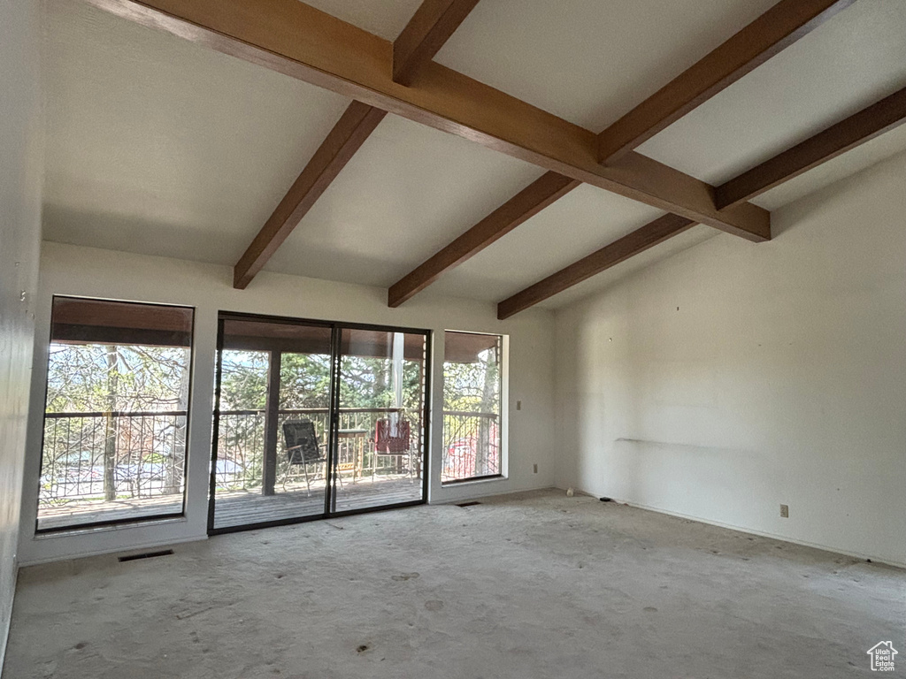 Unfurnished room with plenty of natural light and vaulted ceiling with beams