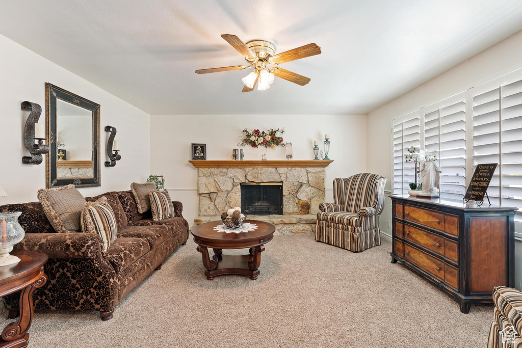 Living room with a stone fireplace, light carpet, and ceiling fan