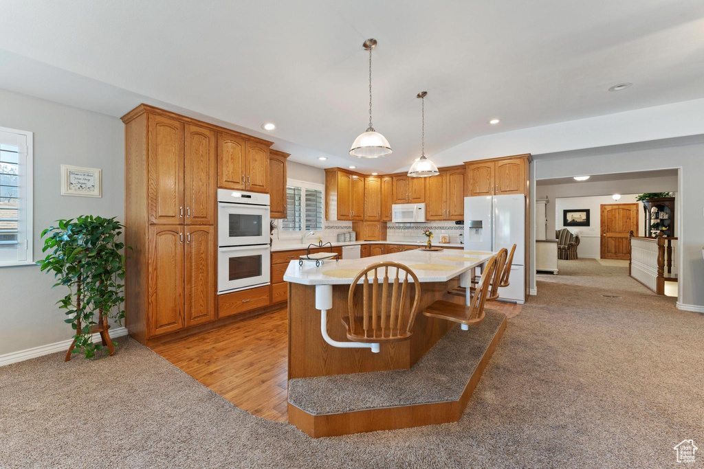 Kitchen with a kitchen bar, light hardwood / wood-style floors, white appliances, decorative light fixtures, and a kitchen island with sink