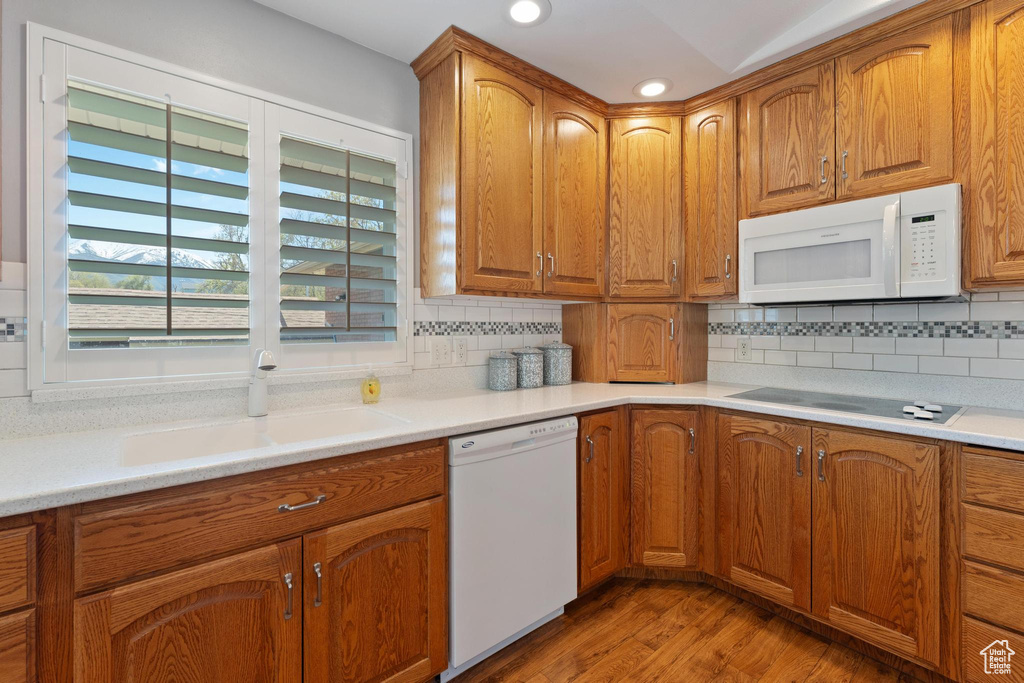 Kitchen featuring tasteful backsplash, wood-type flooring, white appliances, and sink