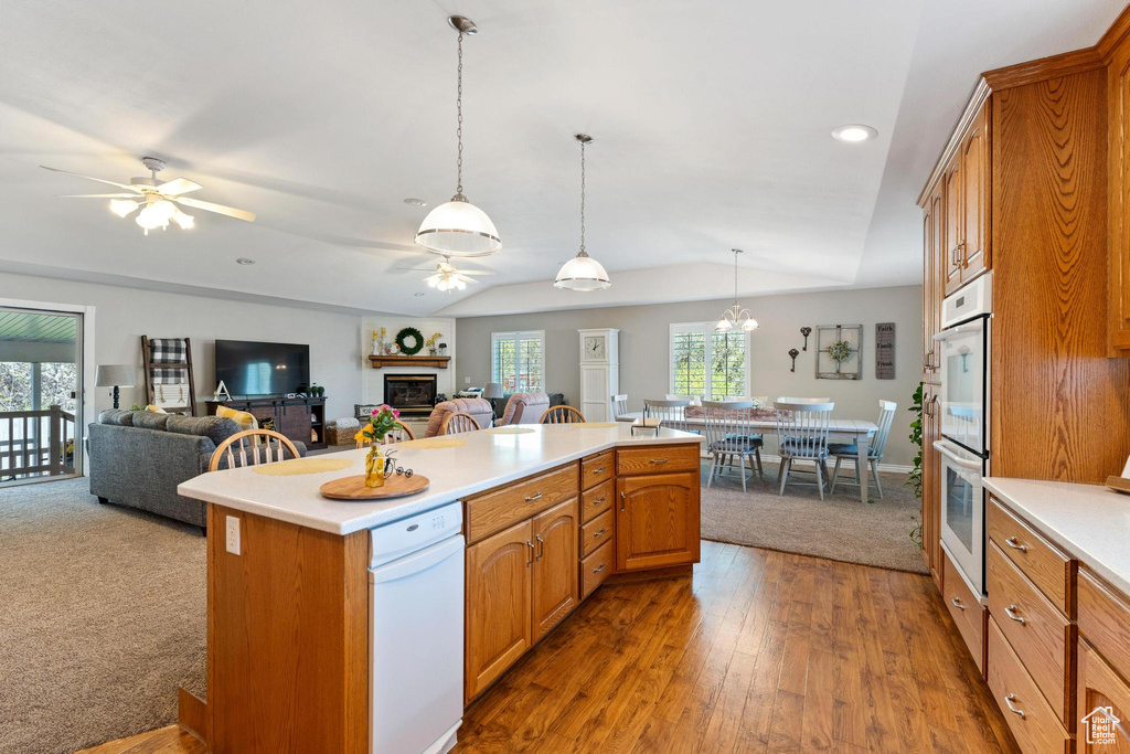 Kitchen with decorative light fixtures, double wall oven, ceiling fan with notable chandelier, light carpet, and a center island