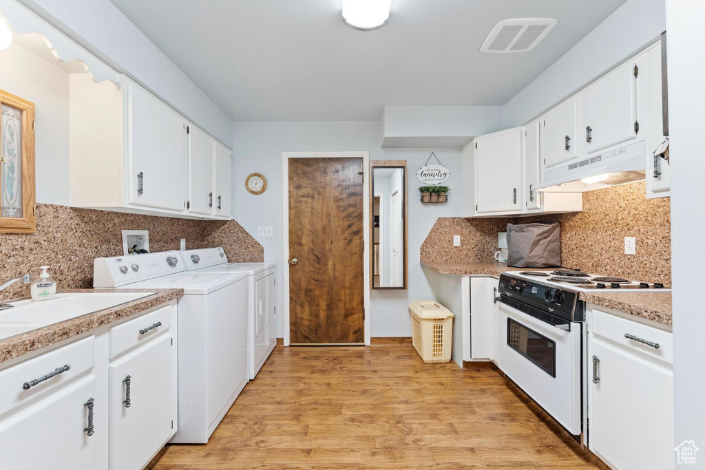 Kitchen featuring white gas range oven, washing machine and clothes dryer, white cabinets, light hardwood / wood-style floors, and premium range hood