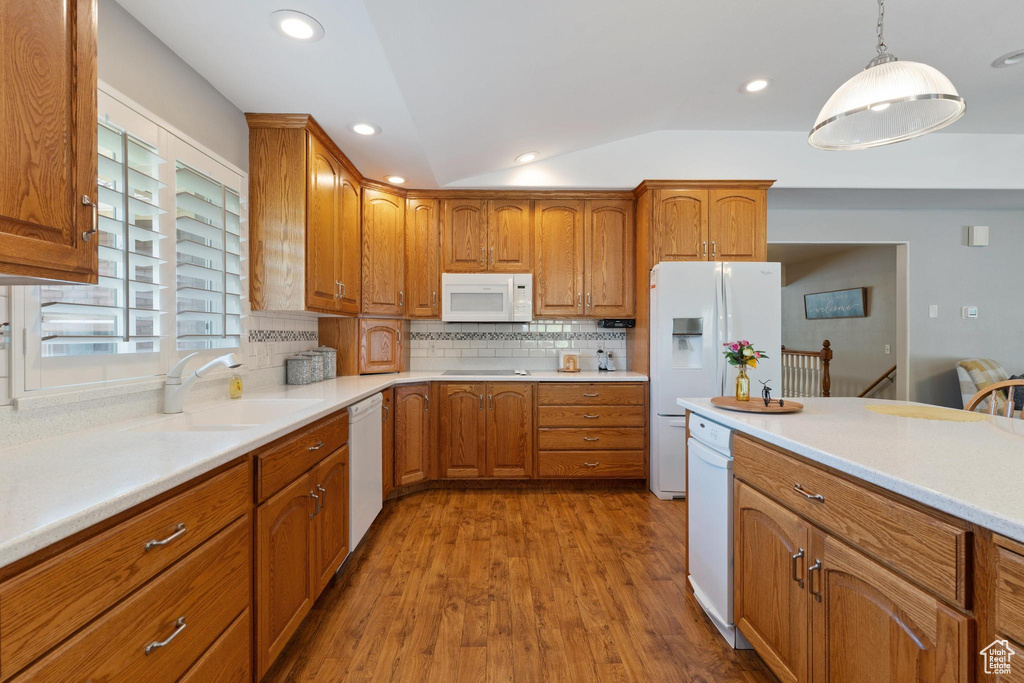 Kitchen featuring sink, white appliances, decorative light fixtures, lofted ceiling, and light hardwood / wood-style flooring