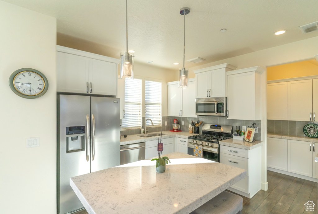 Kitchen featuring decorative light fixtures, stainless steel appliances, white cabinetry, sink, and a center island