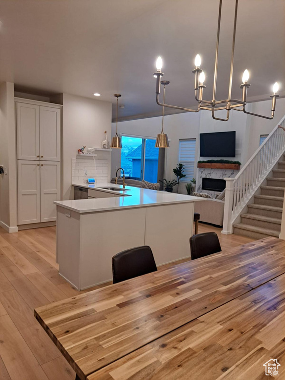 Kitchen with sink, tasteful backsplash, white cabinetry, decorative light fixtures, and light hardwood / wood-style flooring