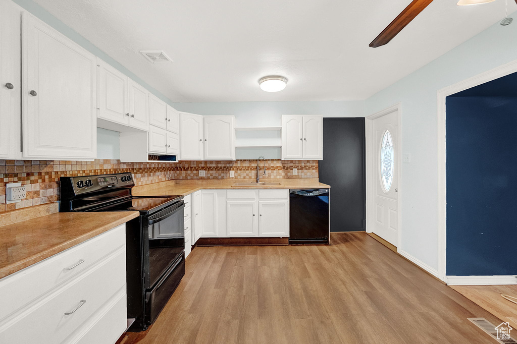 Kitchen with light hardwood / wood-style flooring, white cabinets, and black appliances