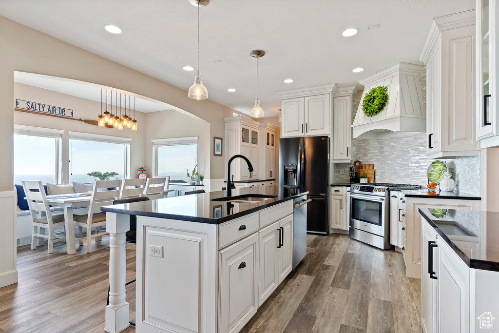 Kitchen featuring appliances with stainless steel finishes, sink, backsplash, a center island with sink, and custom range hood