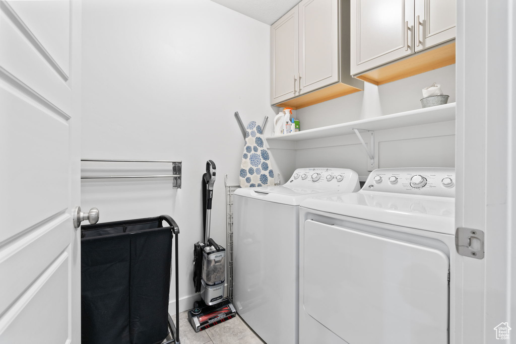 Clothes washing area featuring light tile flooring, cabinets, and separate washer and dryer