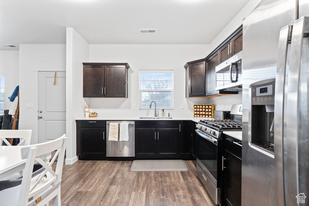 Kitchen featuring sink, stainless steel appliances, dark brown cabinetry, and hardwood / wood-style floors