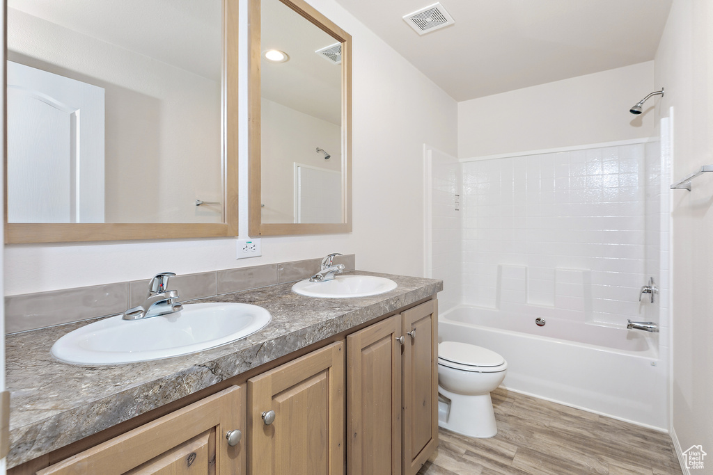 Full bathroom featuring vanity with extensive cabinet space, dual sinks, hardwood / wood-style floors, washtub / shower combination, and toilet