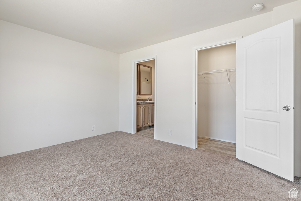 Unfurnished bedroom featuring light carpet, a closet, ensuite bath, and a spacious closet