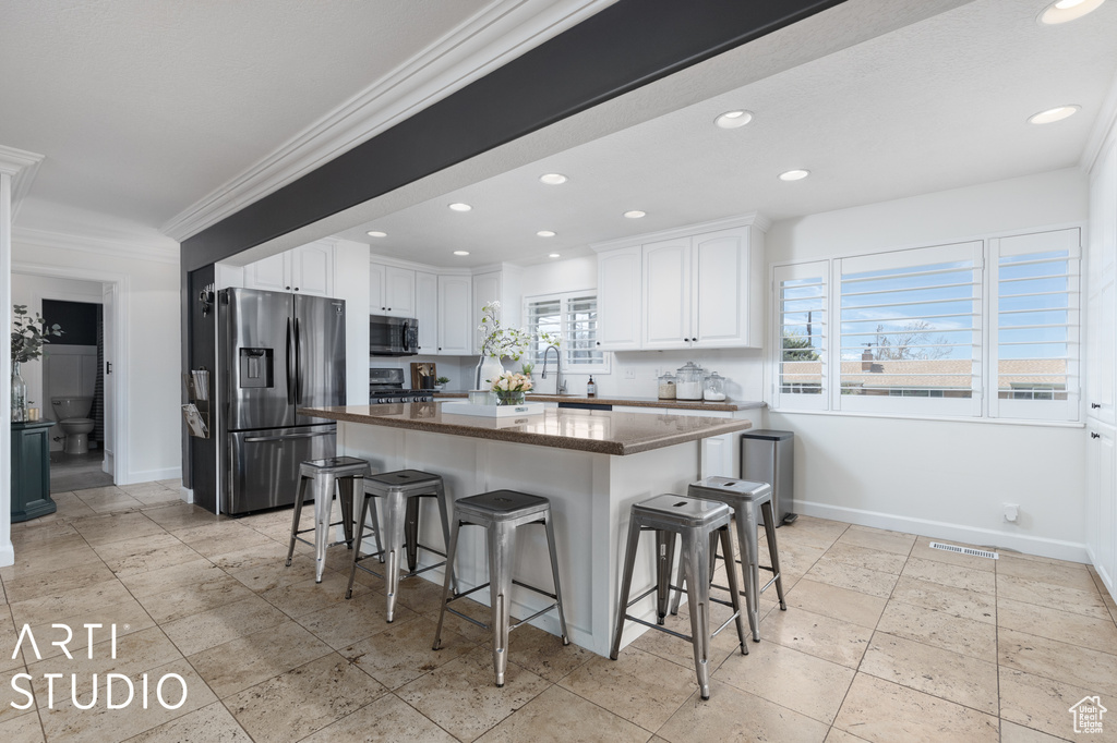 Kitchen featuring white cabinets, a center island, appliances with stainless steel finishes, and a kitchen bar