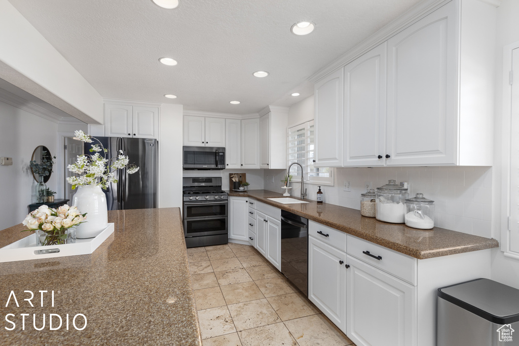 Kitchen featuring dark stone countertops, stainless steel appliances, white cabinetry, and sink