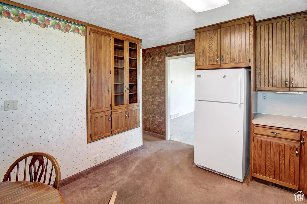 Kitchen featuring light carpet, white fridge, and a textured ceiling