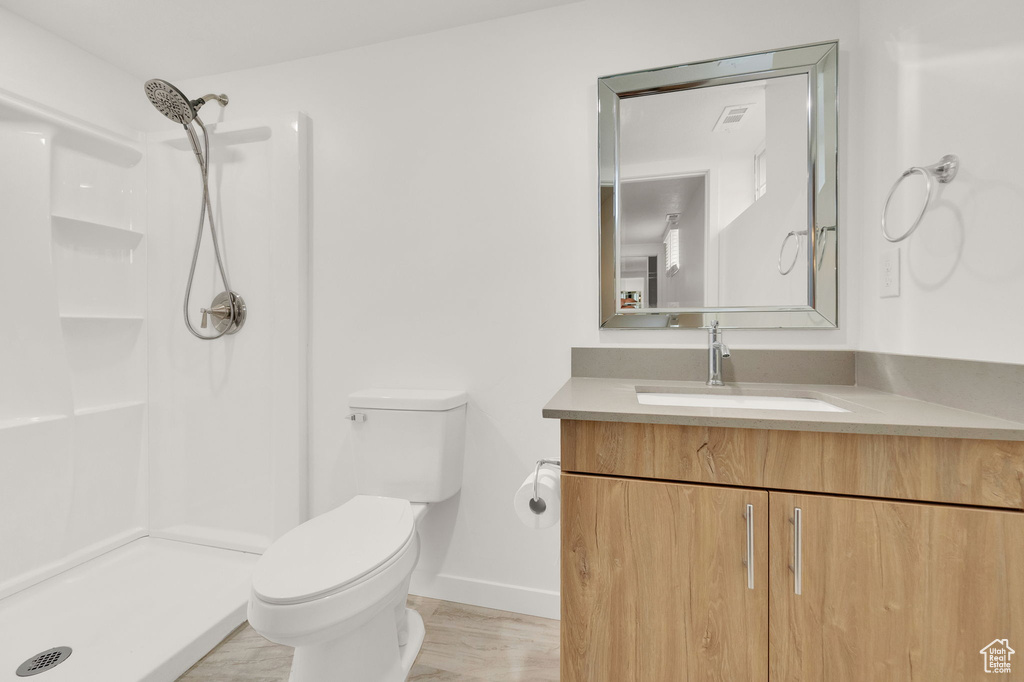 Bathroom with hardwood / wood-style floors, walk in shower, vanity, and toilet