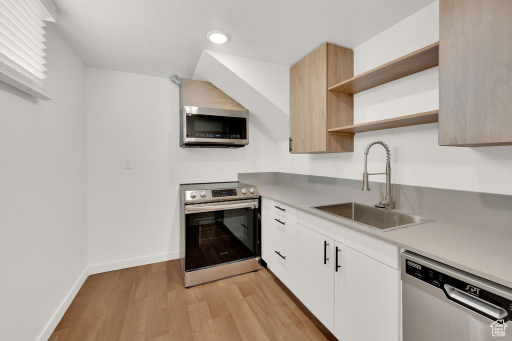 Kitchen with appliances with stainless steel finishes, sink, light wood-type flooring, and white cabinetry