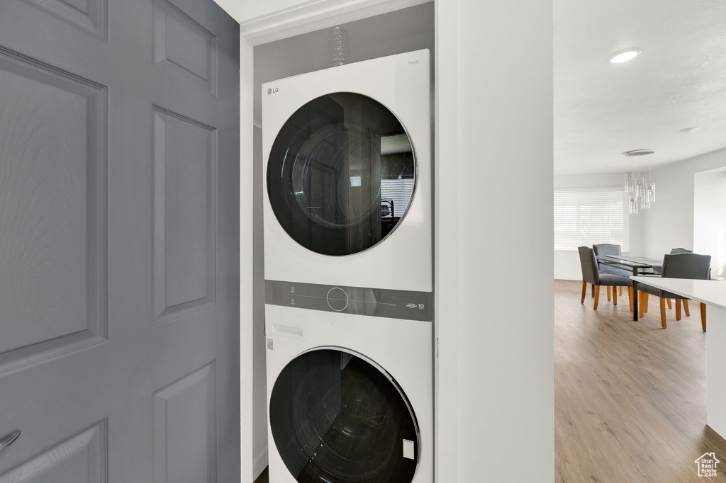 Laundry room featuring light wood-type flooring, stacked washer and dryer, and a chandelier