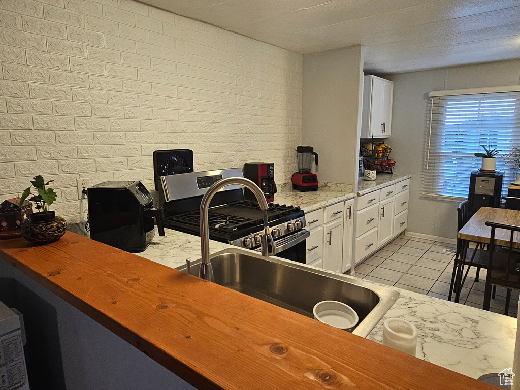 Interior space with brick wall, white cabinets, light tile flooring, and gas stove