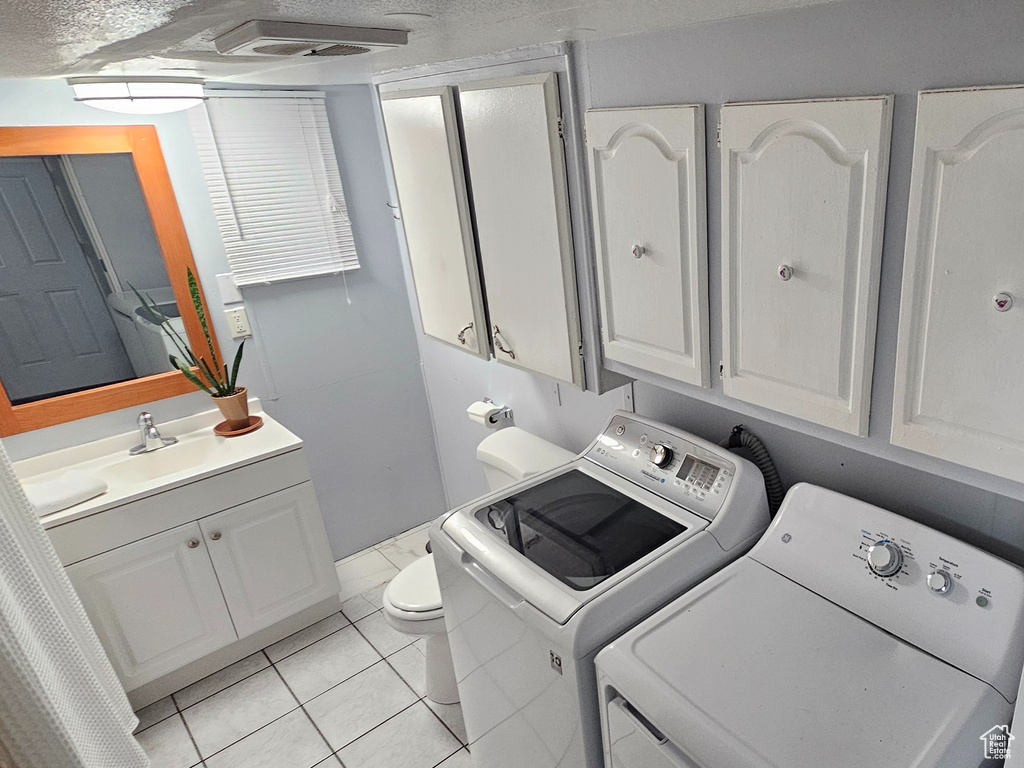 Washroom with sink, light tile floors, separate washer and dryer, and a textured ceiling