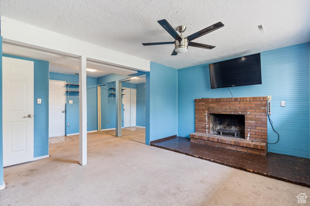 Interior space with light carpet, ceiling fan, a textured ceiling, and a fireplace