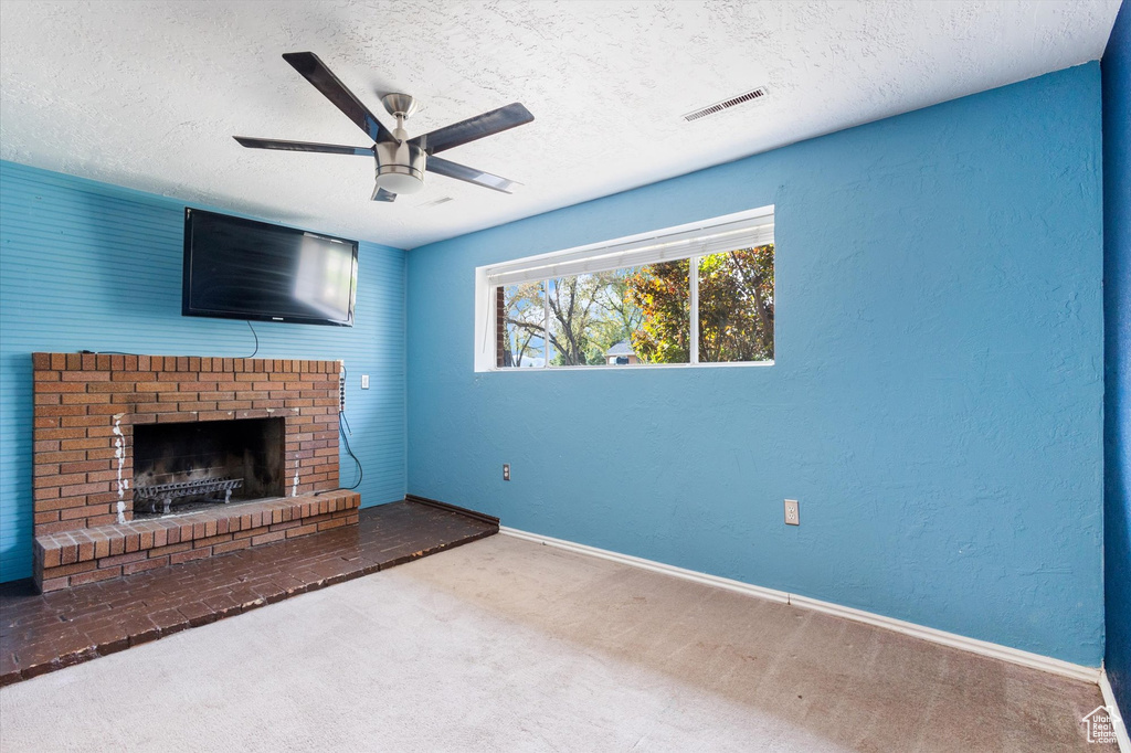 Unfurnished living room with ceiling fan, carpet, a fireplace, and a textured ceiling