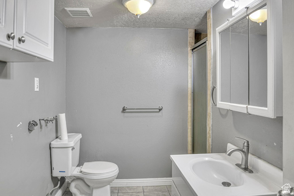 Bathroom with a textured ceiling, toilet, tile floors, and sink