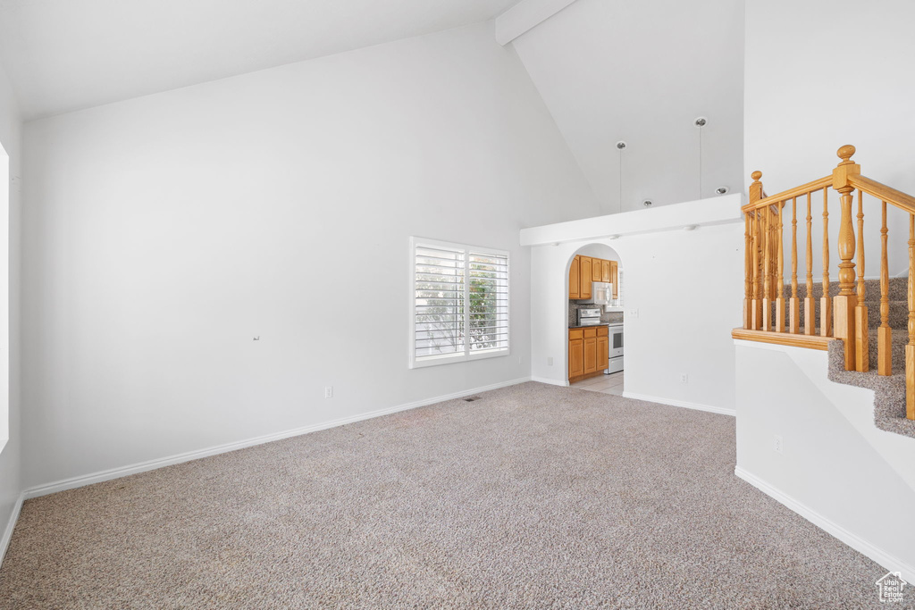 Unfurnished living room with light colored carpet, beam ceiling, and high vaulted ceiling
