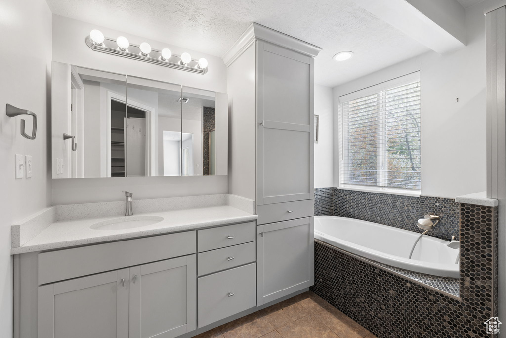 Bathroom featuring a textured ceiling, tile flooring, vanity, and tiled bath