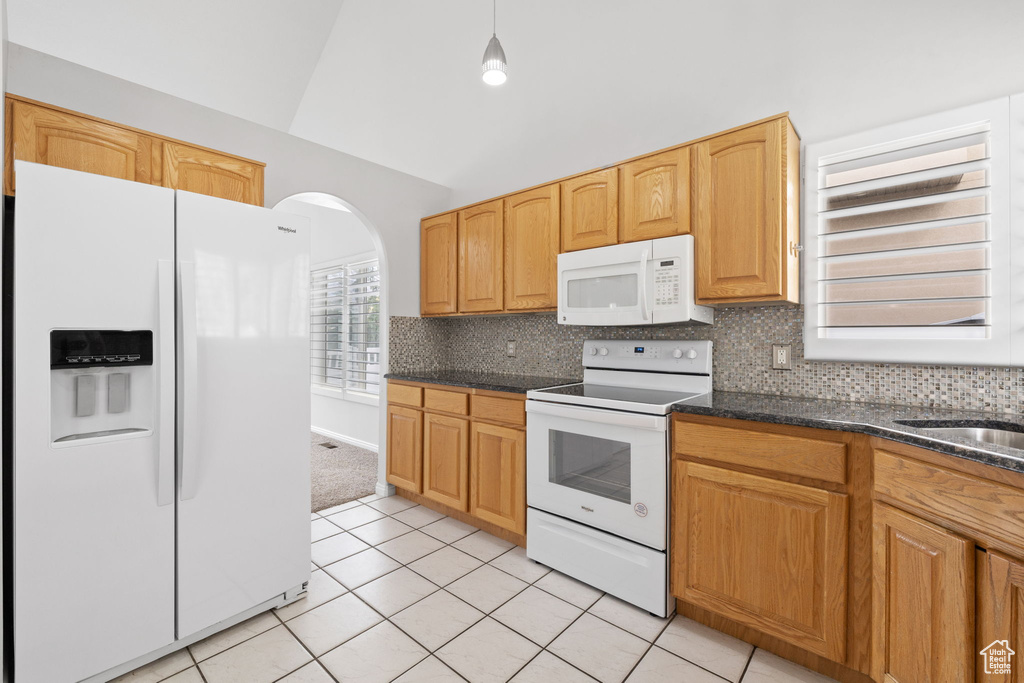 Kitchen with decorative light fixtures, white appliances, tasteful backsplash, and dark stone counters