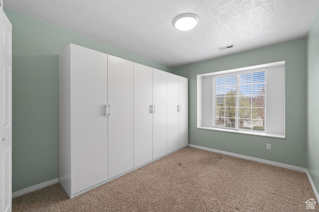 Unfurnished bedroom with light colored carpet, a closet, and a textured ceiling
