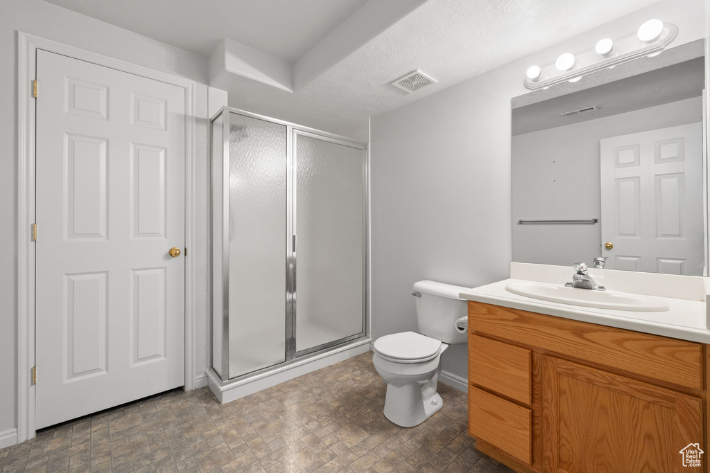 Bathroom with vanity with extensive cabinet space, a shower with door, toilet, and tile flooring