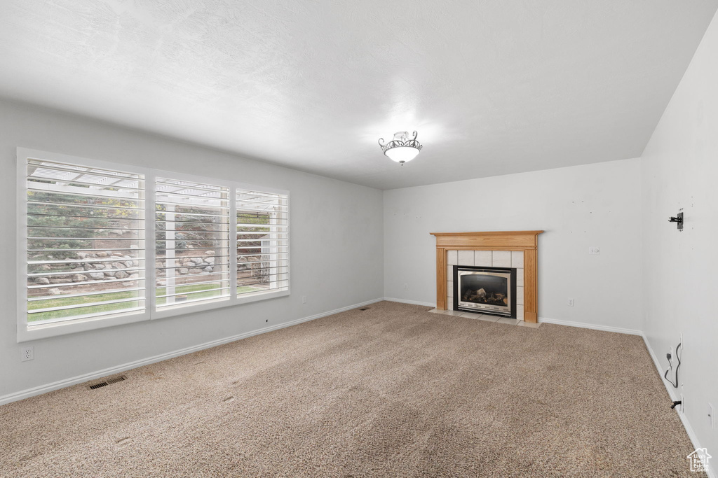 Unfurnished living room featuring light colored carpet, a fireplace, and a wealth of natural light