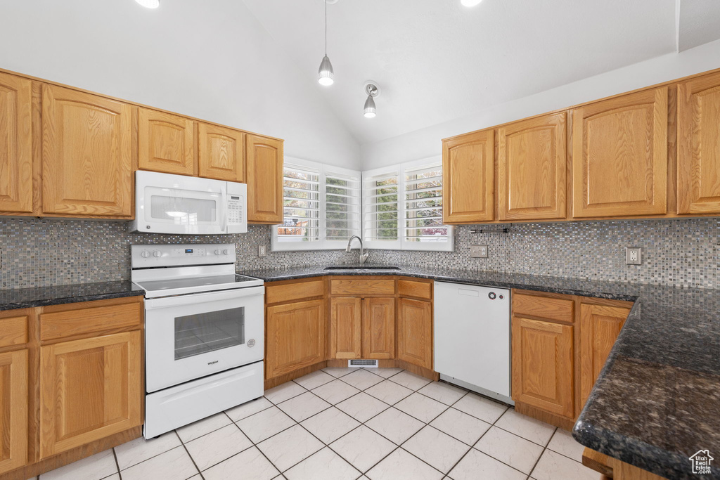 Kitchen featuring tasteful backsplash, dark stone countertops, white appliances, and light tile floors